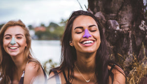 Stylish girls wearing trendy colorful SPF sunscreen on their nose in nature to prevent sun damage